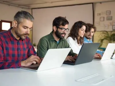 trabajadores hombres y mujeres sentados frente a su laptop